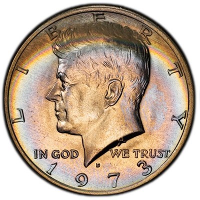 1973 Kennedy Half Dollar with natural rainbow toning showing iridescent bands of amber, blue, and gold radiating across the obverse fields toward the rim